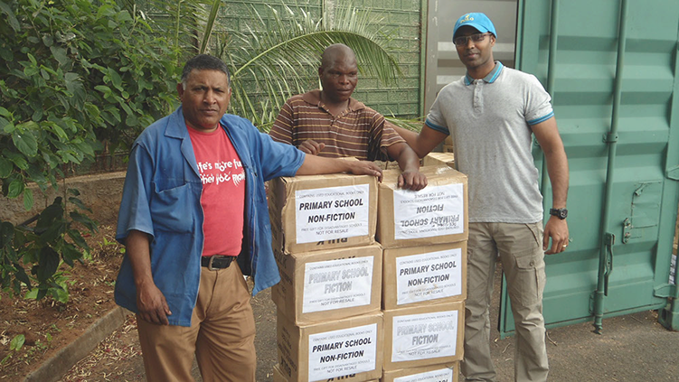 3 African men with a stack of boxed books. All three men leaning on the stack of boxes.