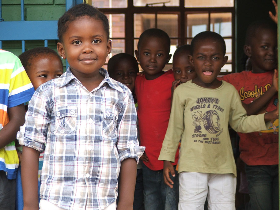 African children smiling at camera, two in the foreground, several in the background. Setting is probably outside a classroom.